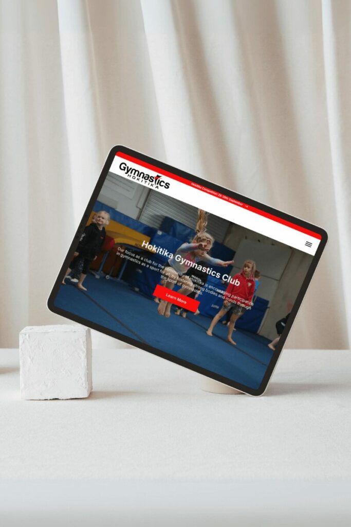 Hokitika Gymnastics website on a tablet sitting with a block holding it up on one side